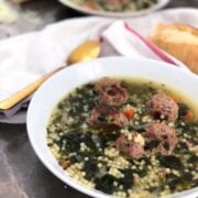 Italian Wedding Soup plated on gray surface with a towel, bread and spoon next to it