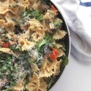 Spicy Sausage Bowtie Pasta in skillet on white table with a white napkin next to it