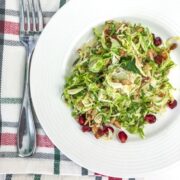 Shaved Brussel Sprout Salad with Honey Dijon Dressing on a white plate with green and red napkin and fork