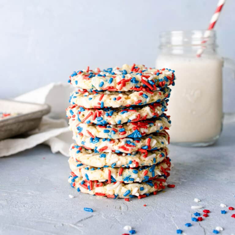 a stack of red white and blue cake mix cookies with a glass of milk in the background