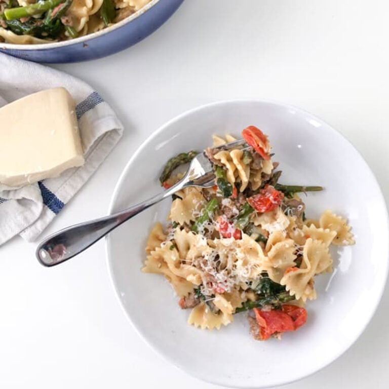 Spicy Sausage Bowtie Pasta in skillet on white table with a white napkin next to it
