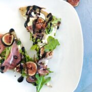 Ricotta Fig Prosciutto Pizza on a white plate and blue background