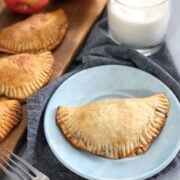apple hand pie on a blue plate with a glass of milk and forks in background
