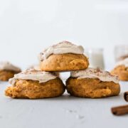3 pumpkin cookies with brown butter icing stacked in a triangle with 3 cinnamon sticks in the foreground