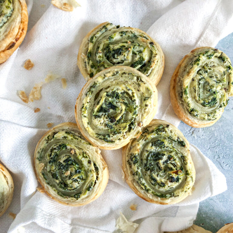 Spinach and Artichoke Puff Pastry Swirls in a pie plate on blue surface
