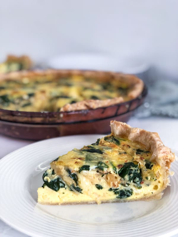 slice of Caramelized Onion & Spinach Quiche on a white plate