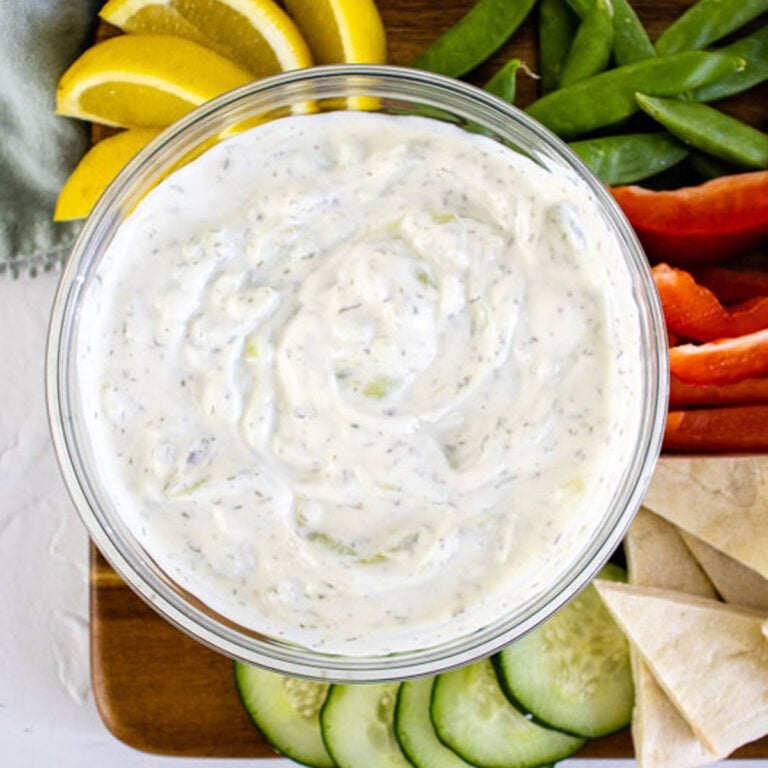 Tzatziki Sauce in a bow in front on gyros and pitas