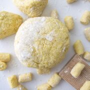 homemade gnocchi dough on a white counter top with sprinkled flour and a gnocchi wooden board