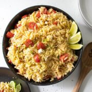 orzo salad in a large black bowl with 2 plates and a wooden spoon next to it
