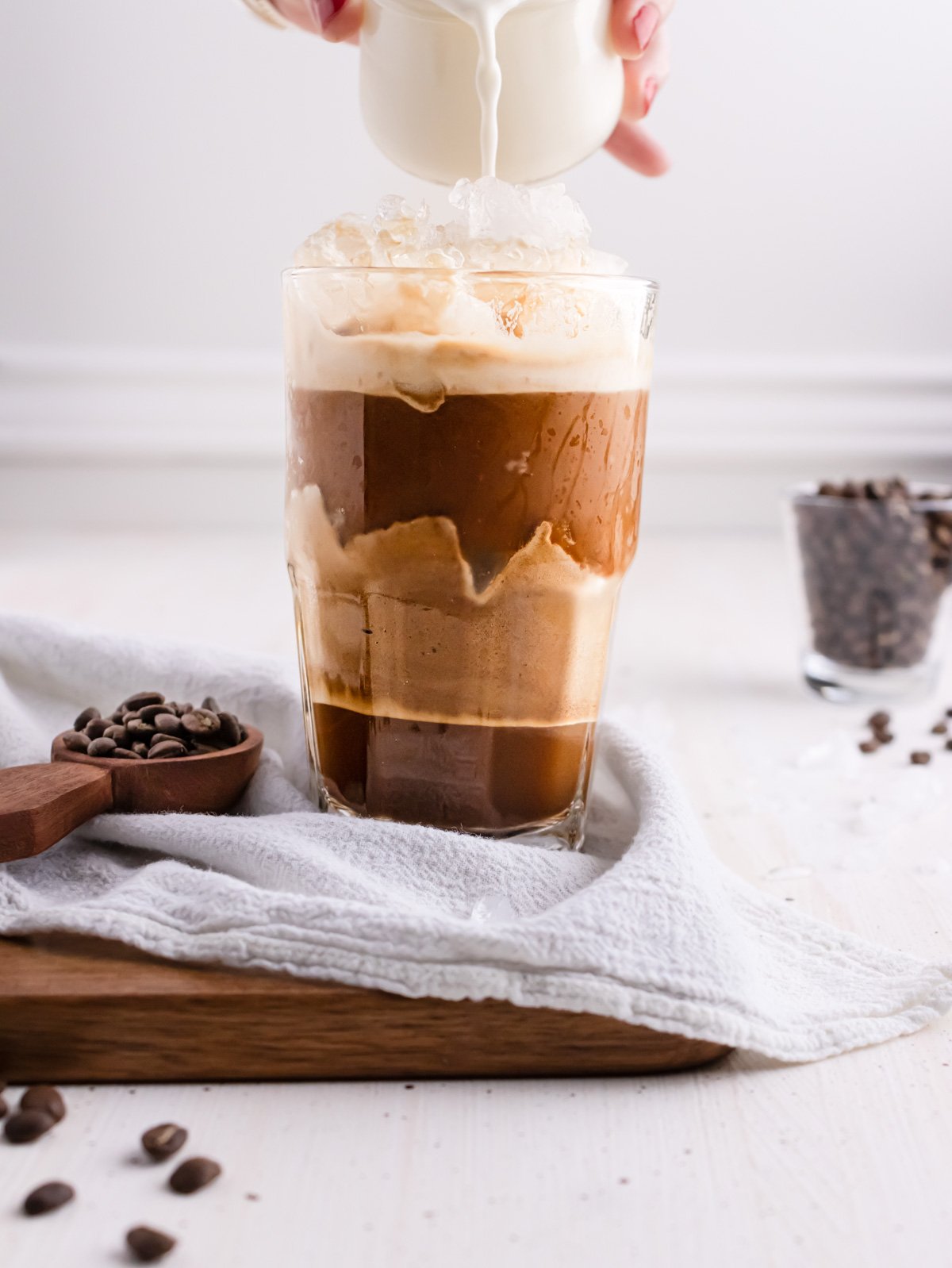 Adding some milk in iced coffee in a clear glass.