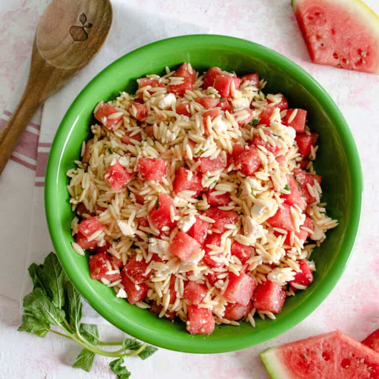 5 Ingredient Watermelon Orzo Salad styled in a green bowl on a pink surface