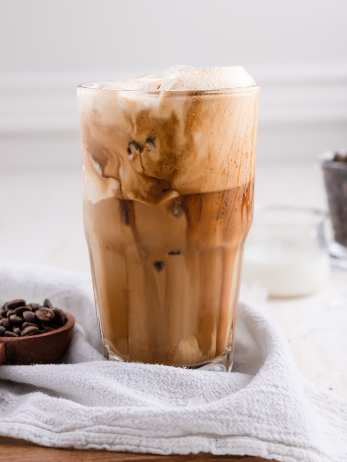 glass of a greek frappe on a white table with coffee beans next to it.
