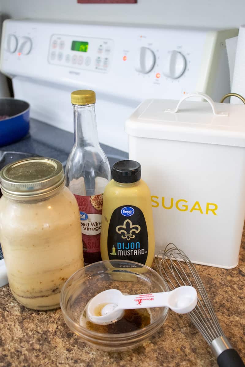 sugar, dijon mustard, bacon grease, red wine vinegar, and a whisk by a stove.