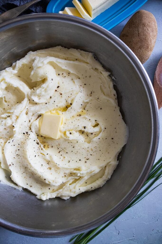 Mashed Potatoes in a silver bowl with a pad of butter on top melting