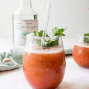 single glass of a frozen watermelon and mint margarita with the tequila bottle in teh background