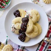 soft butter cookies on a white plate with christmas ribbon, napkin, and lights around it