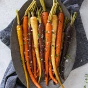 rainbow colored carrots on a silver tray on top of a blue linen napkin sprinkled withs sea salt on top