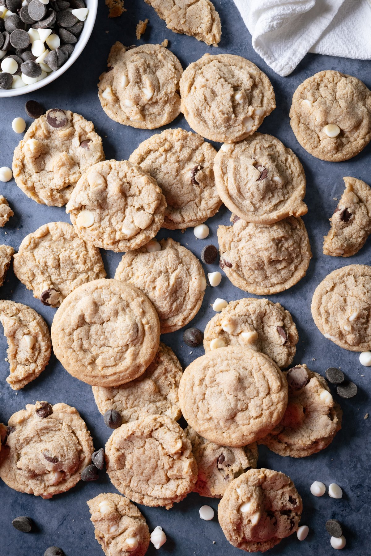 no chill chocolate chip cookies all scattered out on a dark background with chocolate chips next to them.