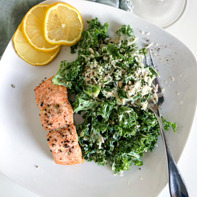 plate of Kale Caesar Salad with Baked Salmon with a fork, glass of wine, and green napkin