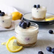 3 mason jars of lemon blueberry cheesecakes with lemon slices and blueberries next to them