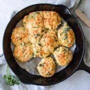 a cast iron skillet of Jalapeno Cheddar Drop Biscuits on a blue towel with a spatula next to it