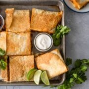 Sheet Pan Quesadilla cut in squares on a baking sheet with avocados, limes, sour cream, and salsa