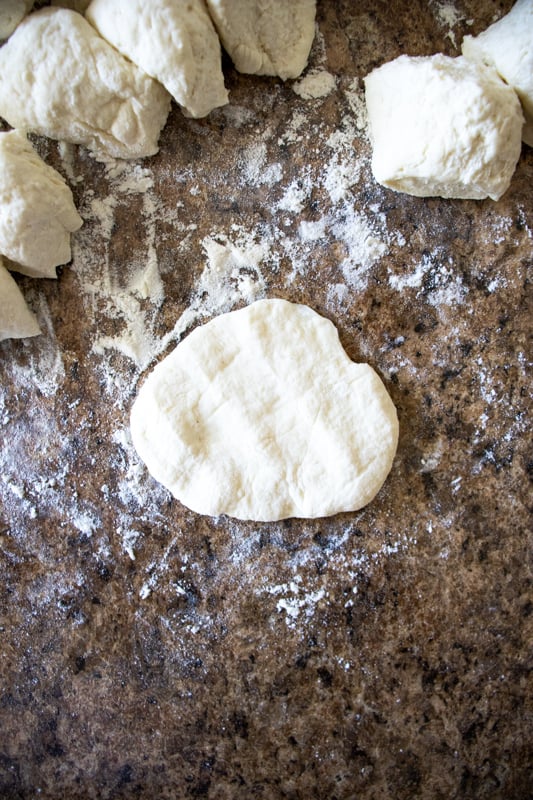 A flattened round of pizza dough on a counter top. 