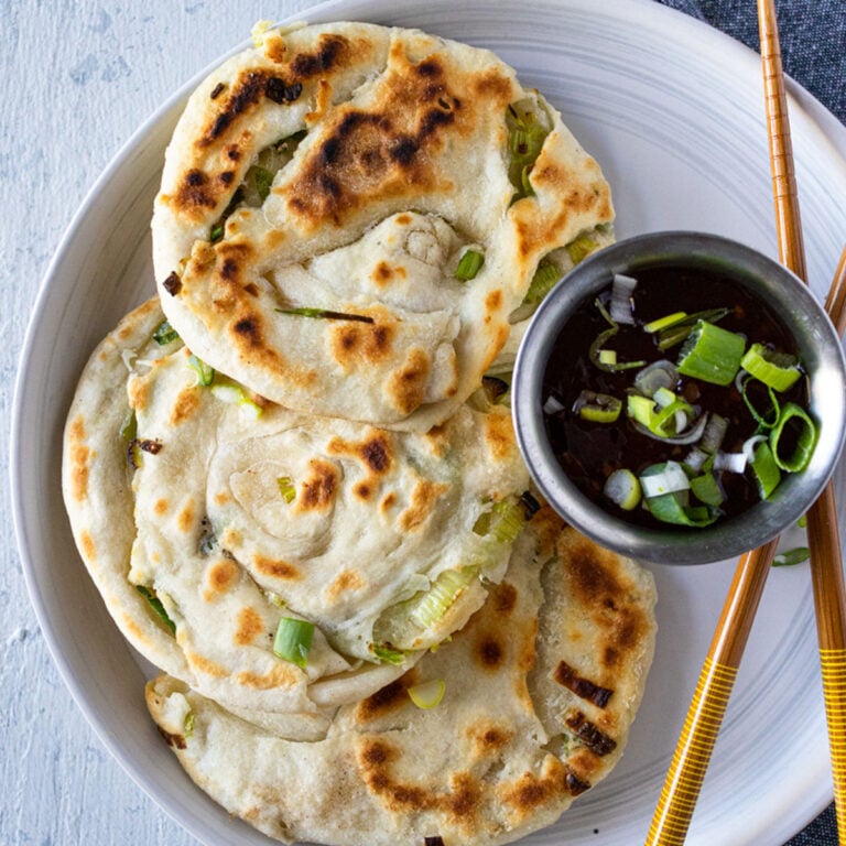 3 scallion pancakes on a white plate with chopsticks and sweet chili sauce