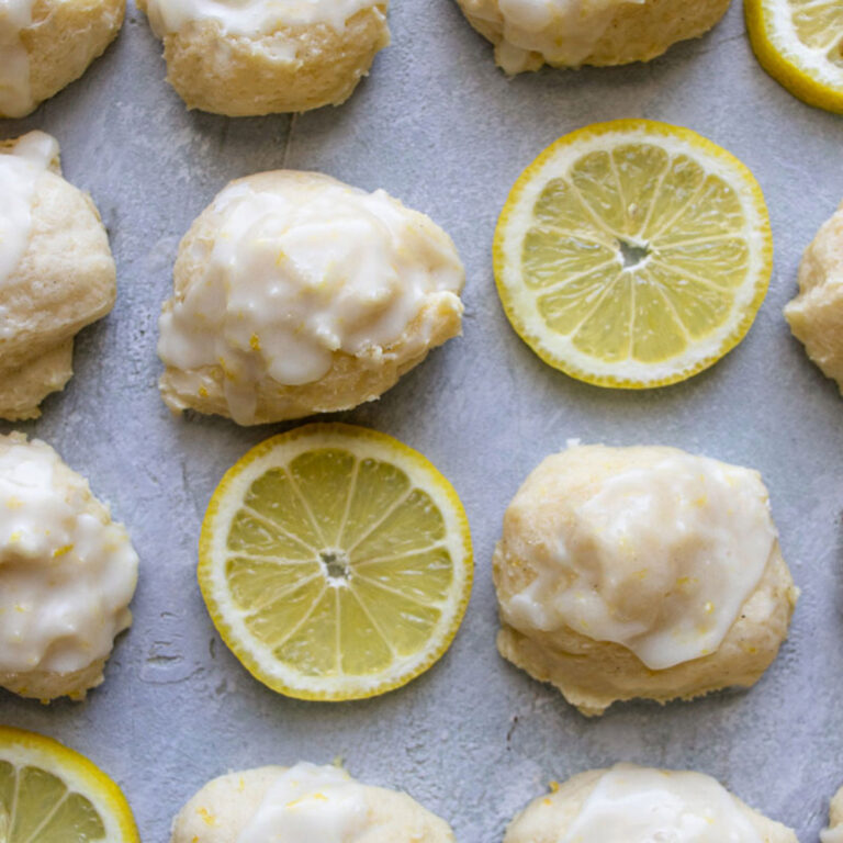 3 lemon ricotta cookies on a plate with lemon wedges and a whisk in the background