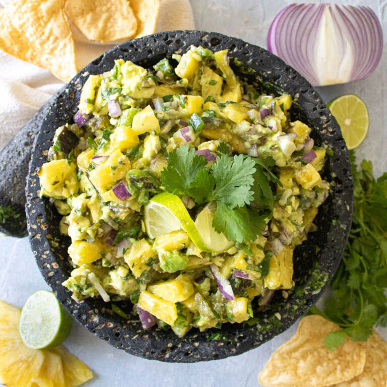 pineapple and poblano salsa wth chips, cilantro, limes, and red onions around it