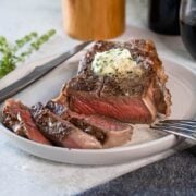 sous vide steak sliced on a plate with a bottle of wine behind it