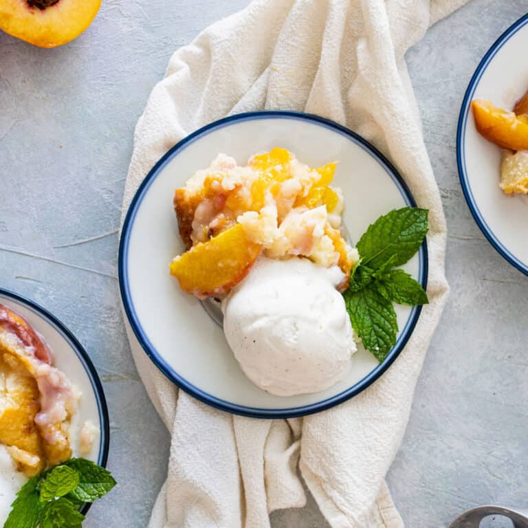 3 plates of peach cobbler with scoops of ice cream and mint on top. sliced peaches, mint and ice cream scoop next to the plates
