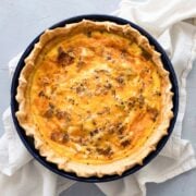 bacon and cheddar quiche in a pie plate with napkin under it