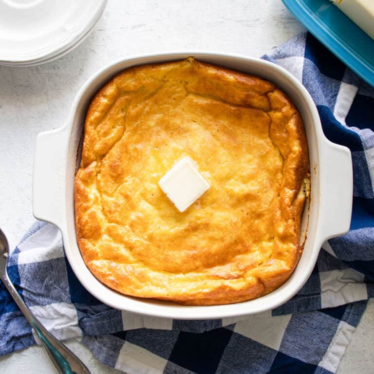 southern spoon bread in a casserole dish with butter and plates next to it.