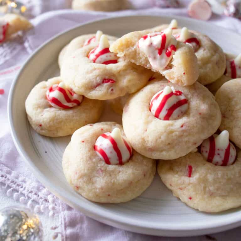 candy cane kiss cookies on a platter with kisses and lights next to it.