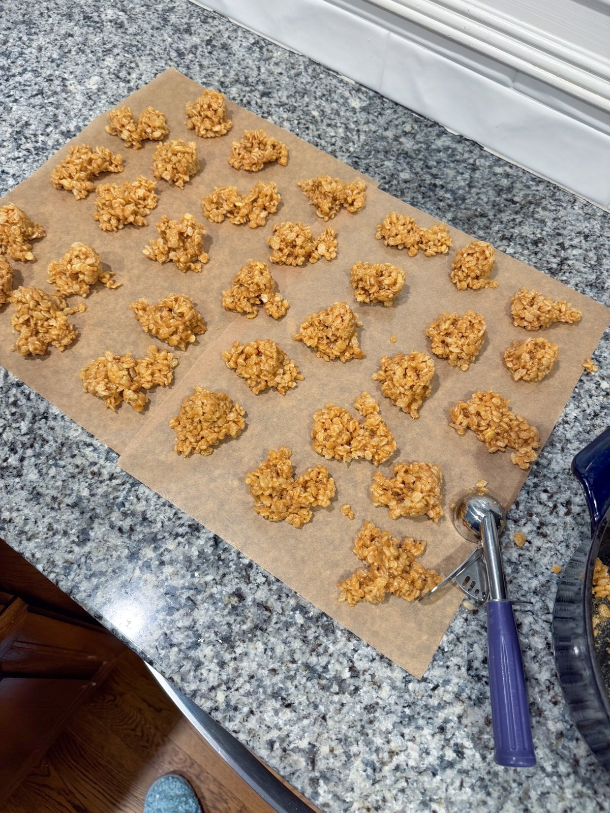 Scooping out peanut butter balls onto parchment paper on a kitchen counter.