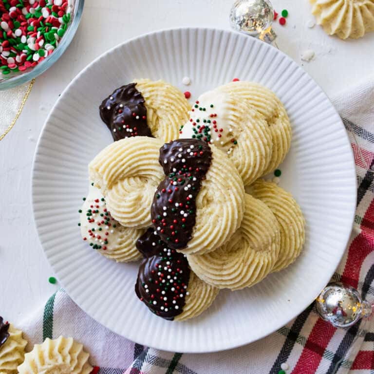 soft butter cookies on a white plate with christmas ribbon, napkin, and lights around it.