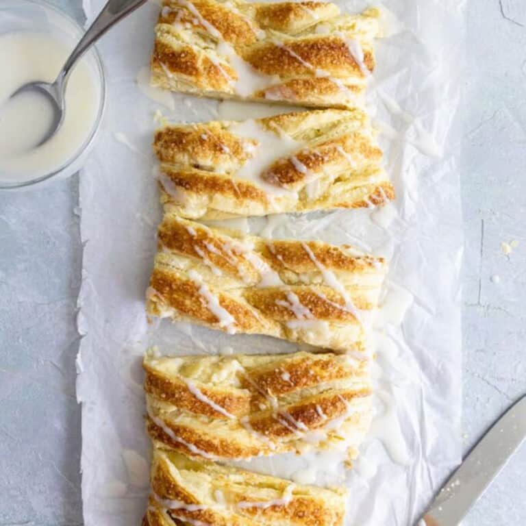 cream cheese danish cut into bites on a blue table with a bowl of icing next to it