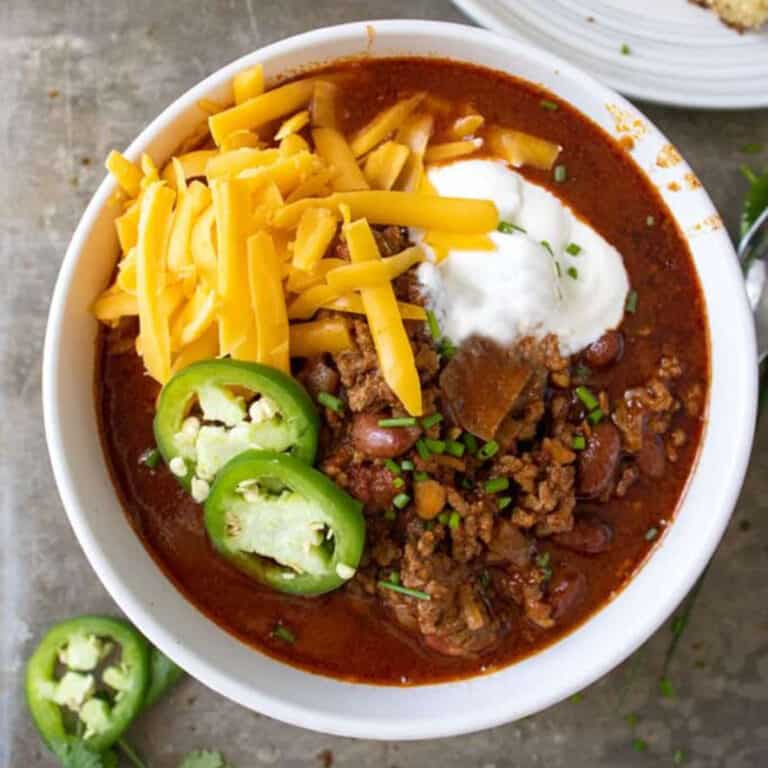 bowl of chili con carne with jalapenos and corn bread around it