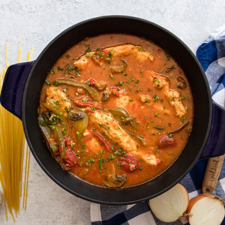 easy chicken cacciatore in a dutch oven with spaghetti and a wooden spoon next to it