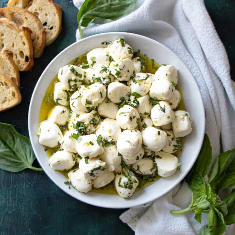 bowl of Easy Marinated Mozzarella Balls with basil and bread next to it.