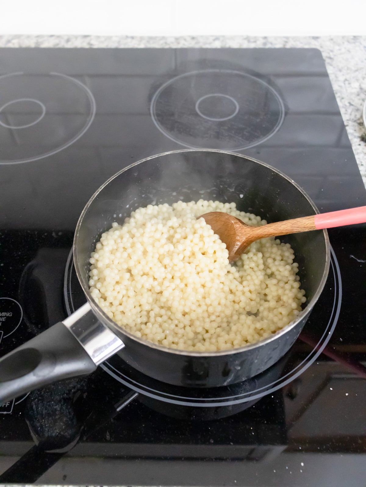 fluffing couscous on the stove with a wooden spoon