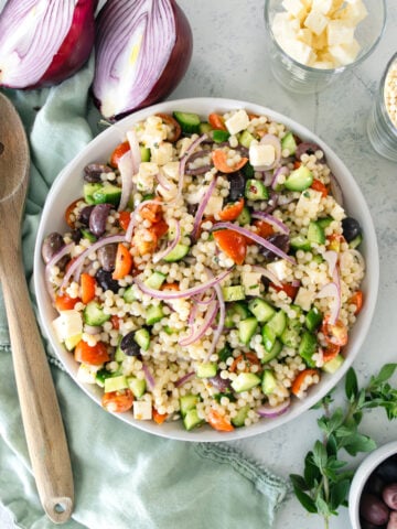 couscous salad in a big serving bowl with a wooden knife next to it.