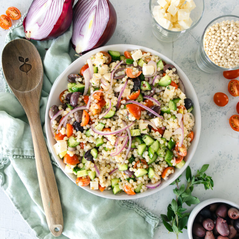 couscous salad in a big serving bowl with a wooden knife next to it.