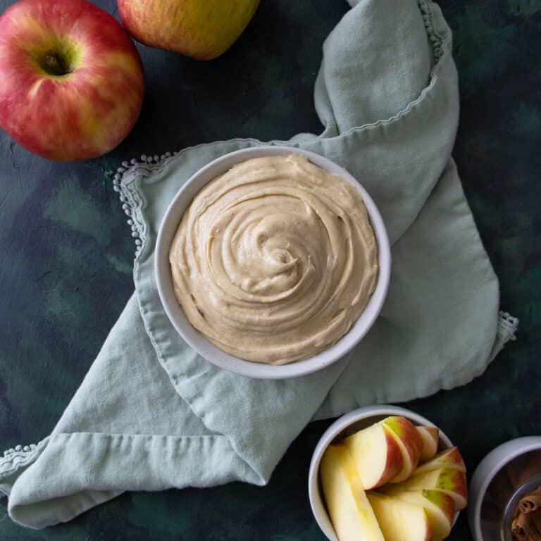 Apple dip in a bowl on top of a green napkin with apples next to it.
