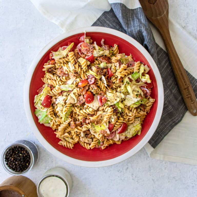 BLT pasta salad in a big bowl with a napkin and wooden spoon next to it.
