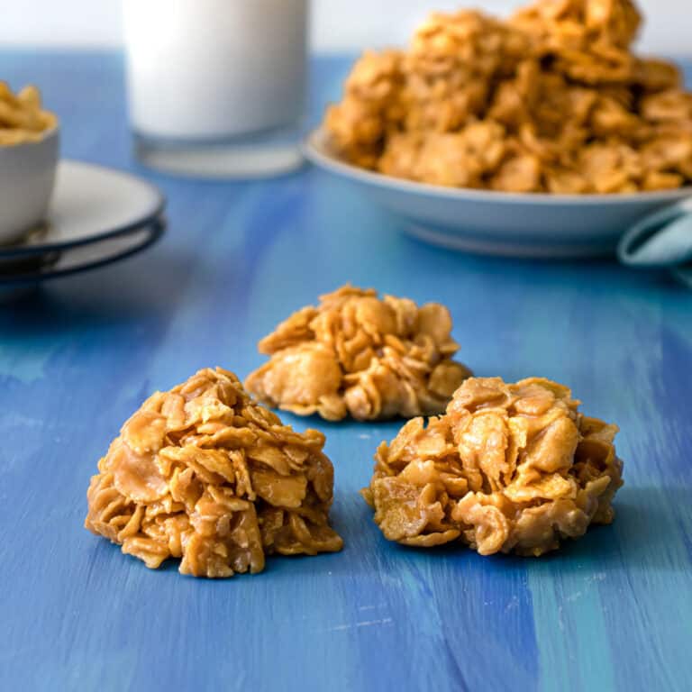 3 Cornflake Peanut Butter Balls {No Bake} on a blue table with a plate of them and a glass of milk in the background.
