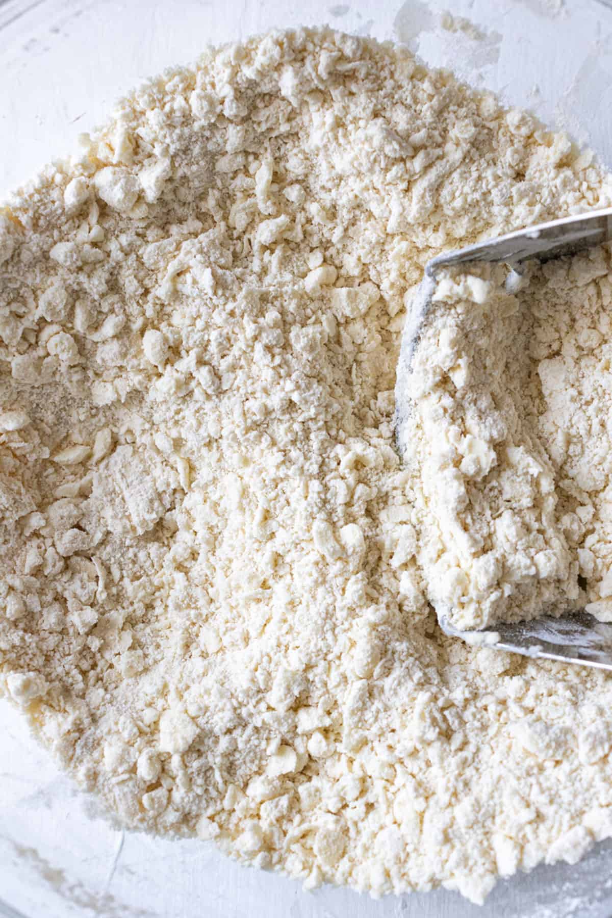 Crumbly dough in a bowl with a pastry knife.