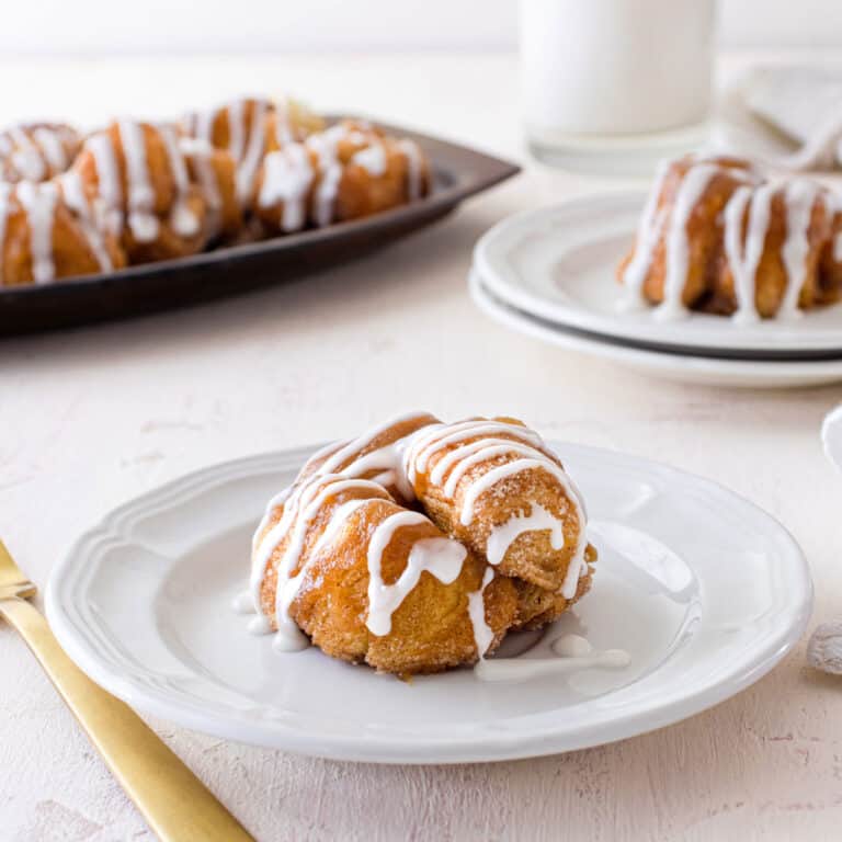 A mini monkey bread muffin on a white plate with a platter of them in the background.