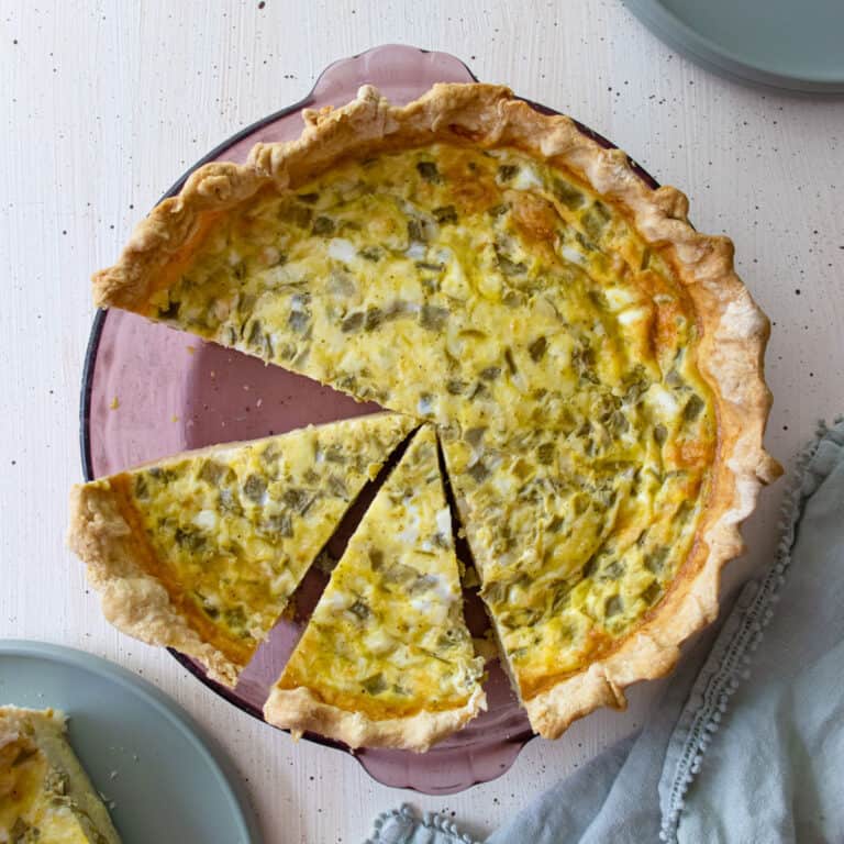 chiles rellenos quiche in a pie dish with 2 slices cut and 1 on a green plate next it the pie plate.